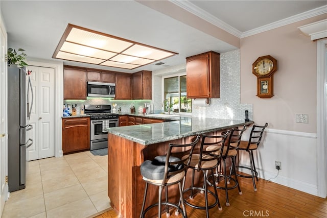 kitchen with sink, kitchen peninsula, crown molding, appliances with stainless steel finishes, and stone counters