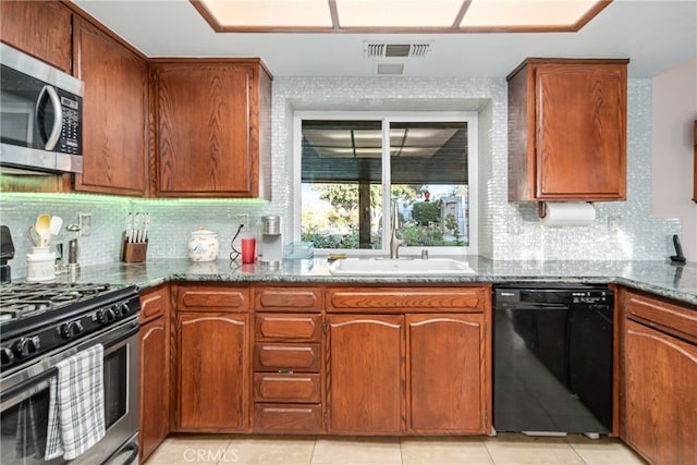 kitchen featuring dark stone countertops, light tile patterned flooring, stainless steel appliances, and sink