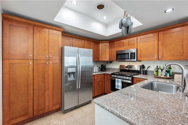 kitchen featuring light stone countertops, appliances with stainless steel finishes, a raised ceiling, sink, and light tile patterned floors