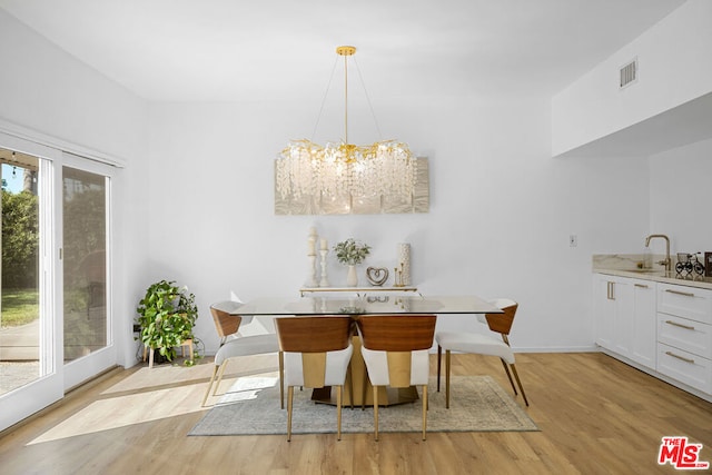 dining room with an inviting chandelier, sink, and light hardwood / wood-style flooring