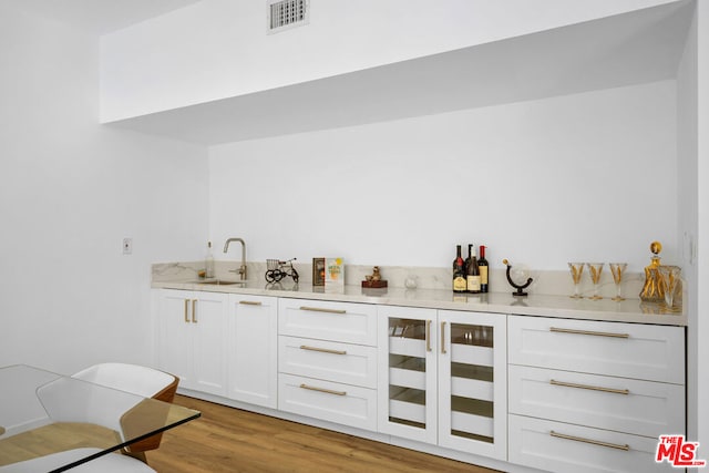 bar featuring light hardwood / wood-style floors, white cabinetry, and sink