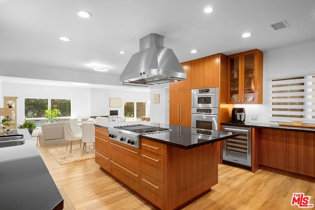 kitchen with island exhaust hood, appliances with stainless steel finishes, beverage cooler, light hardwood / wood-style floors, and a kitchen island