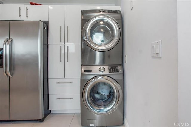 washroom featuring cabinets, stacked washer / dryer, and light tile patterned flooring