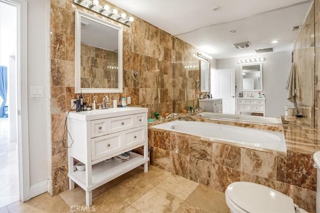 bathroom with vanity, a relaxing tiled tub, toilet, and tile walls