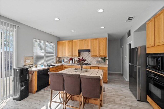 kitchen featuring a center island, tile counters, a healthy amount of sunlight, and black appliances