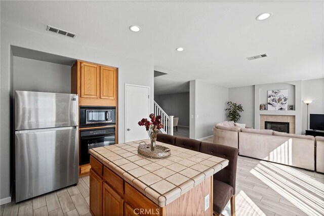 kitchen with black appliances, light wood-type flooring, a fireplace, tile counters, and a kitchen island