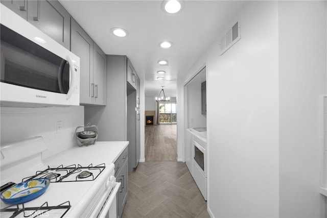 kitchen featuring light parquet floors, gray cabinetry, an inviting chandelier, and white appliances