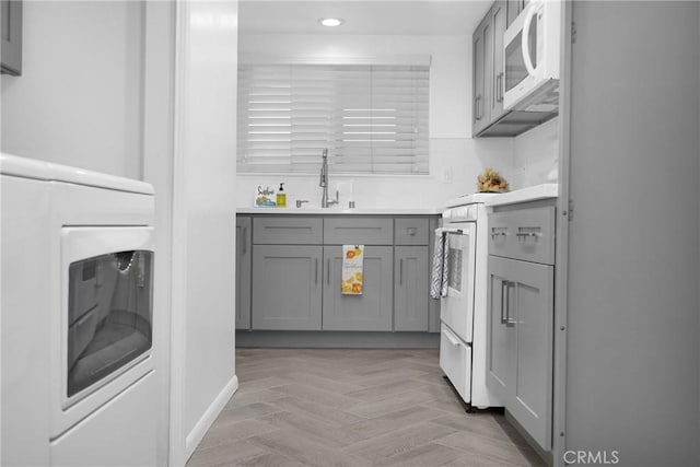 kitchen with washer / dryer, light parquet floors, gray cabinets, range, and sink