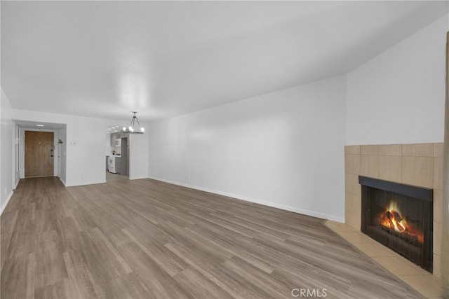 unfurnished living room featuring a notable chandelier, a tile fireplace, and light hardwood / wood-style floors