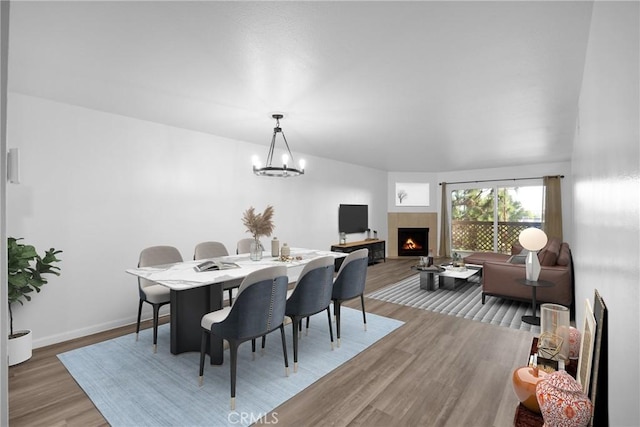 dining space featuring a tiled fireplace, a chandelier, and wood-type flooring