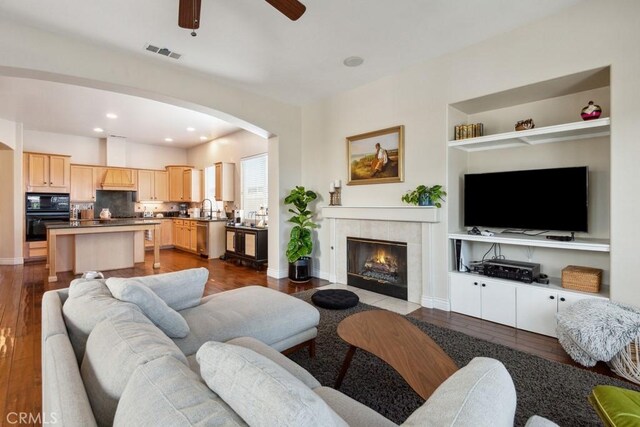 living room featuring a tile fireplace, light hardwood / wood-style flooring, ceiling fan, and sink