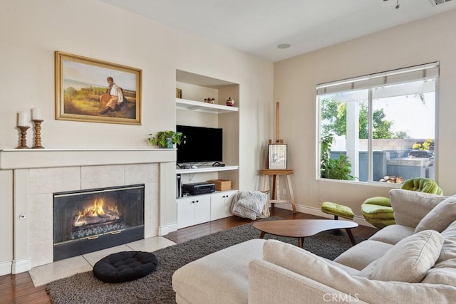 living room with a tiled fireplace, built in shelves, and light wood-type flooring