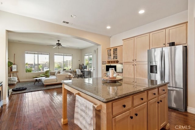 kitchen with ceiling fan, a center island, stainless steel fridge with ice dispenser, dark hardwood / wood-style floors, and dark stone counters