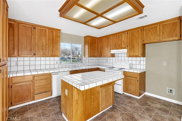 kitchen featuring white appliances, visible vents, tile counters, brown cabinets, and a center island