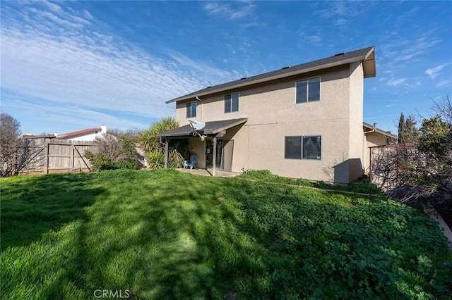 rear view of property with stucco siding, a lawn, and fence