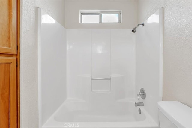 bathroom featuring shower / washtub combination, a textured wall, and toilet