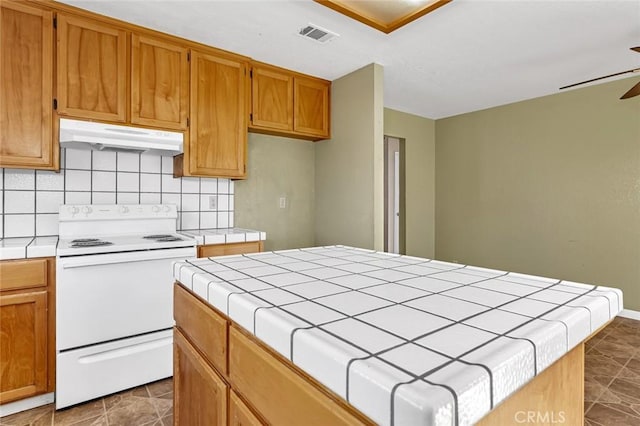 kitchen featuring electric stove, tile countertops, a kitchen island, ceiling fan, and under cabinet range hood