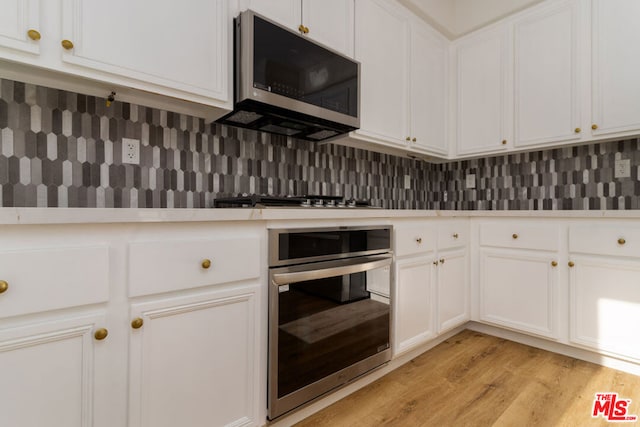 kitchen featuring white cabinets, appliances with stainless steel finishes, light wood-type flooring, and backsplash