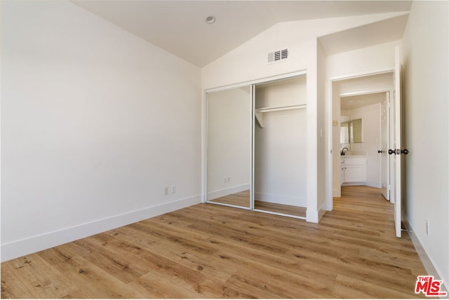 unfurnished bedroom with wood-type flooring, vaulted ceiling, and a closet