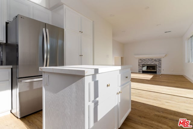 kitchen featuring white cabinetry, a stone fireplace, stainless steel fridge, a kitchen island, and light wood-type flooring