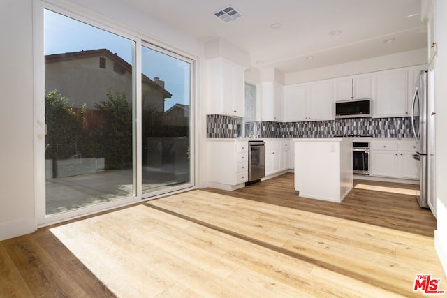 kitchen featuring white cabinets, wood-type flooring, decorative backsplash, a kitchen island, and appliances with stainless steel finishes