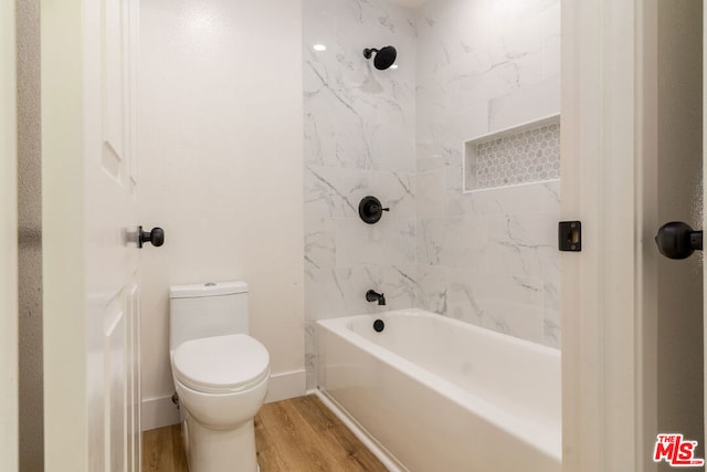 bathroom with wood-type flooring, tiled shower / bath combo, and toilet