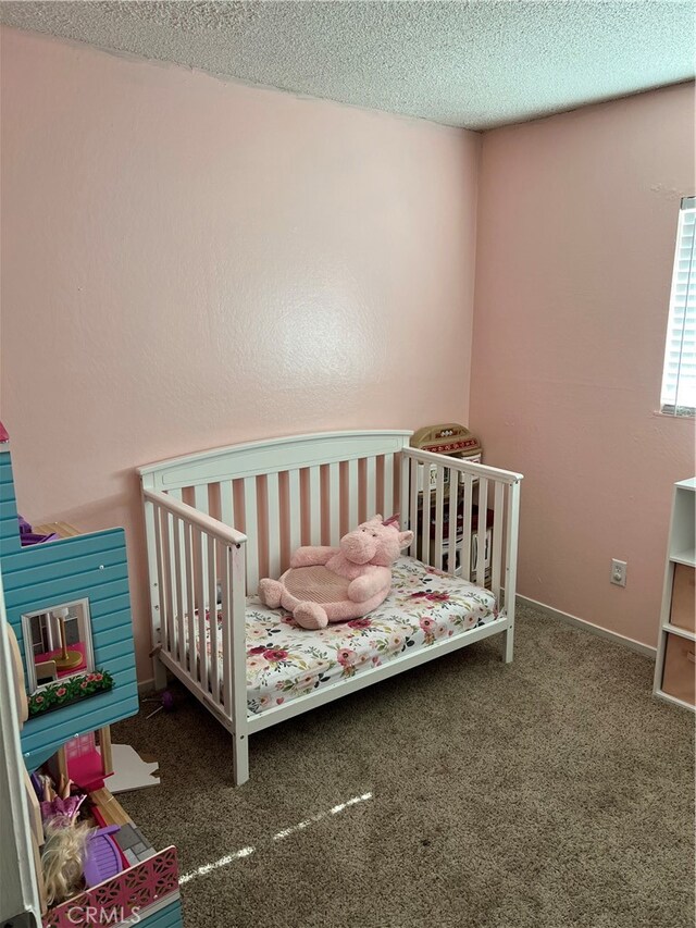 carpeted bedroom featuring a nursery area and a textured ceiling