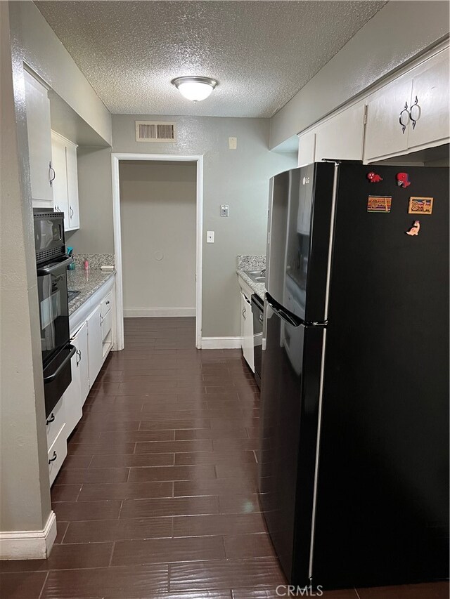 kitchen featuring light stone countertops, black appliances, a textured ceiling, dark hardwood / wood-style flooring, and white cabinetry