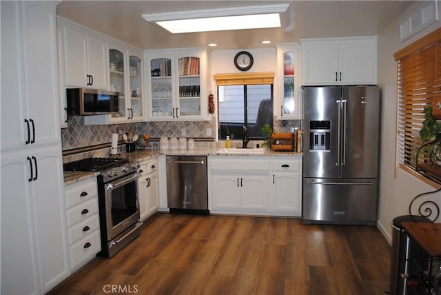 kitchen with light stone counters, white cabinets, dark wood-type flooring, and appliances with stainless steel finishes