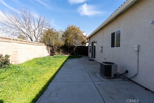 view of side of property featuring a yard, a patio, stucco siding, central AC unit, and a fenced backyard