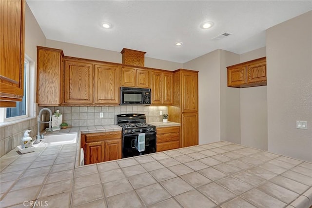 kitchen featuring a sink, visible vents, tile counters, decorative backsplash, and black appliances