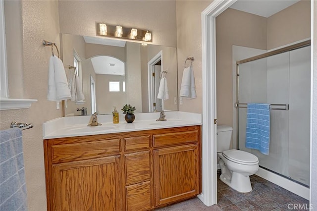 bathroom featuring toilet, a shower stall, double vanity, and a sink