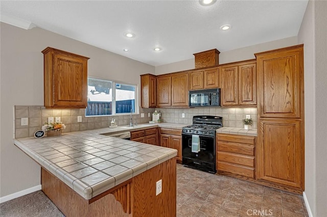 kitchen with tile countertops, black appliances, tasteful backsplash, and a peninsula