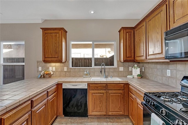 kitchen featuring tile countertops, a sink, brown cabinets, black appliances, and tasteful backsplash