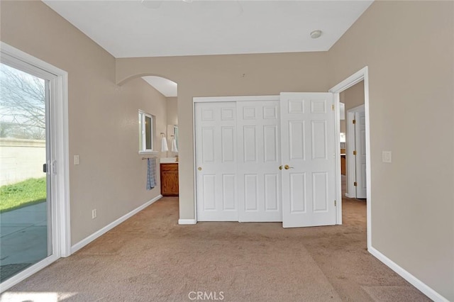 unfurnished bedroom with arched walkways, baseboards, carpet, access to outside, and a closet