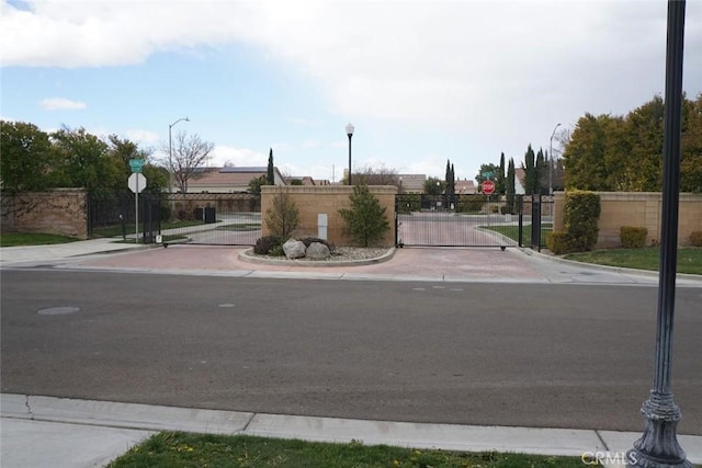 view of road with a gated entry, curbs, traffic signs, a gate, and street lights