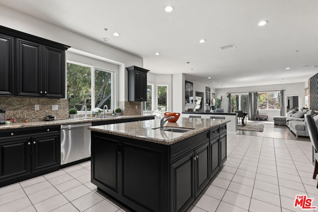 kitchen with decorative backsplash, light stone counters, sink, dishwasher, and an island with sink