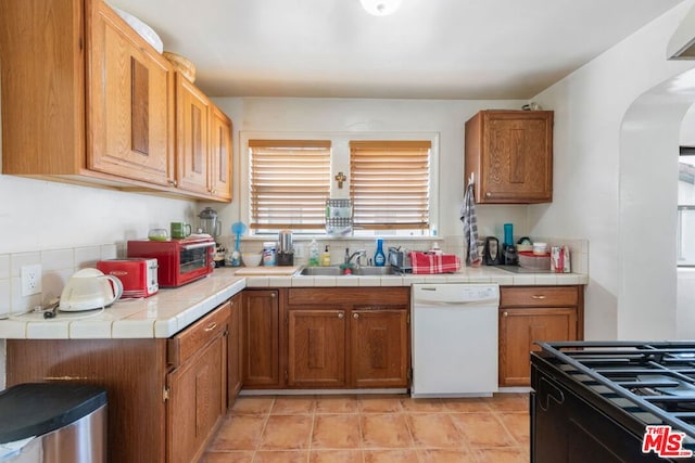 kitchen featuring light tile patterned flooring, black range, sink, dishwasher, and tile countertops