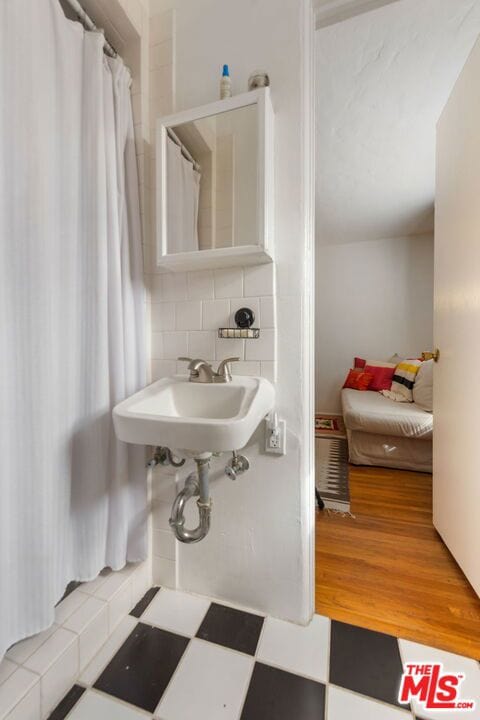 bathroom with wood-type flooring, curtained shower, sink, and decorative backsplash