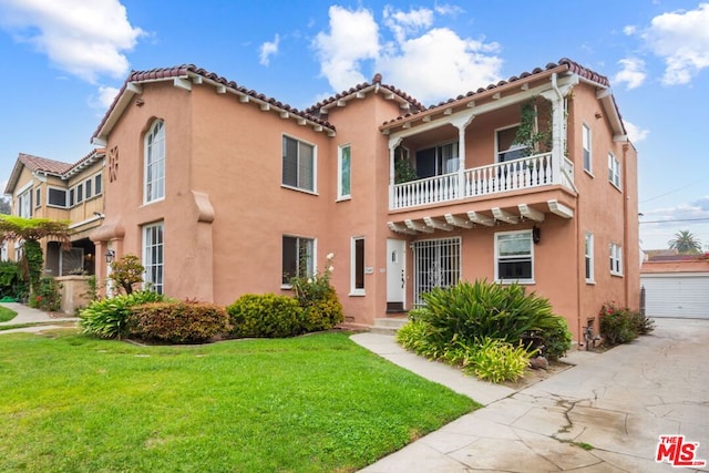 mediterranean / spanish-style home featuring a front yard, a garage, a balcony, and an outdoor structure