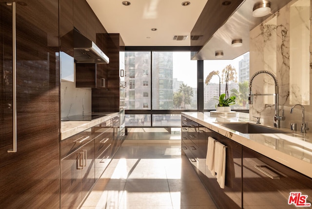 kitchen with black electric stovetop, wall chimney range hood, tile patterned flooring, dark brown cabinets, and sink