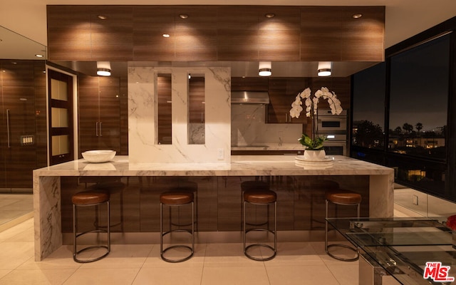 bar with extractor fan, double oven, and light tile patterned floors