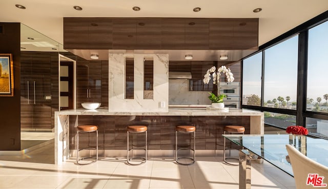 bar with expansive windows, tasteful backsplash, light tile patterned flooring, and stainless steel double oven