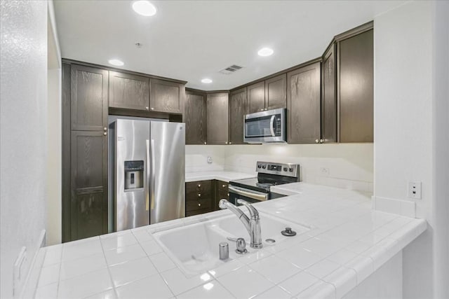 kitchen with stainless steel appliances, tile countertops, dark brown cabinets, and sink