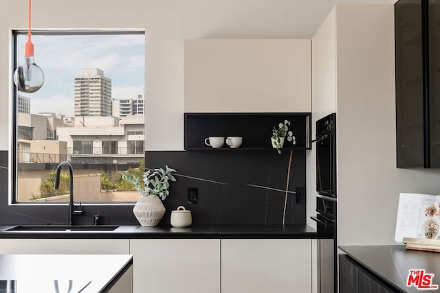 kitchen with oven, white cabinetry, and sink