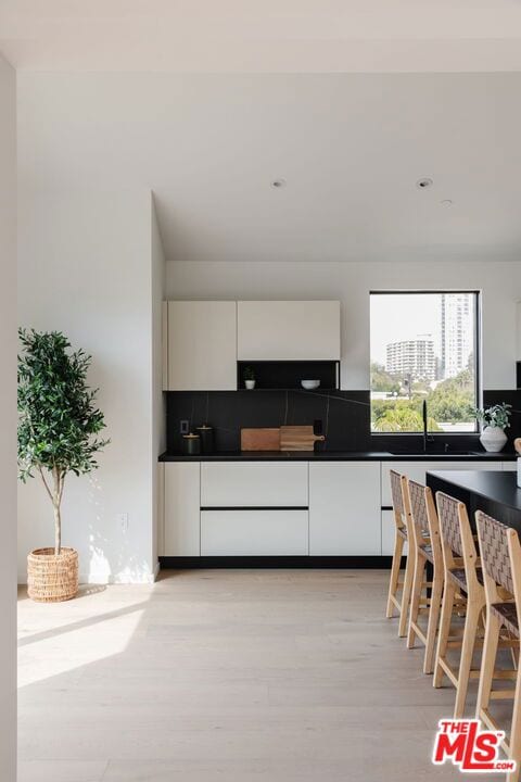 kitchen with sink, white cabinetry, light hardwood / wood-style flooring, and tasteful backsplash