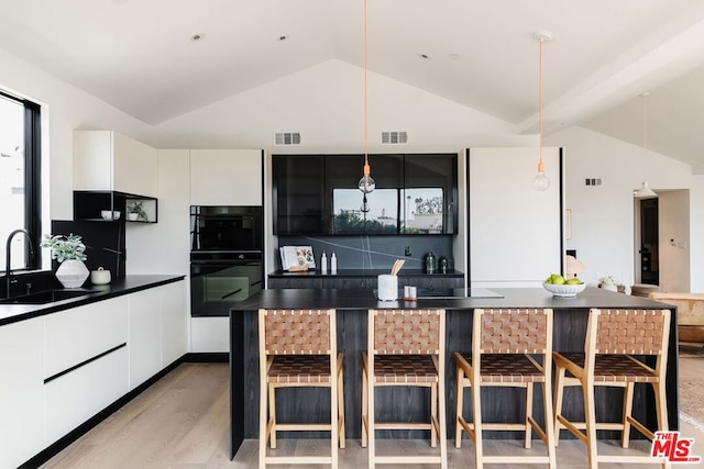 kitchen featuring white cabinets, a kitchen breakfast bar, sink, double oven, and light hardwood / wood-style floors