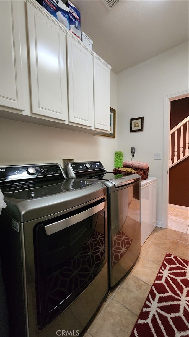 clothes washing area featuring light tile patterned flooring, washer and dryer, and cabinets