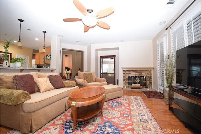 living room with a fireplace, light wood-type flooring, and ceiling fan