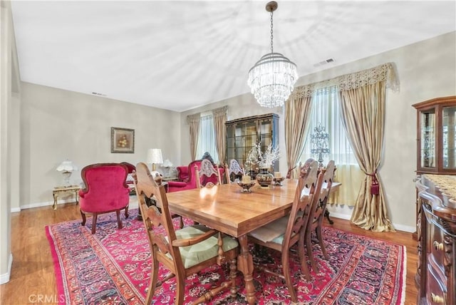 dining area featuring visible vents, a notable chandelier, baseboards, and wood finished floors